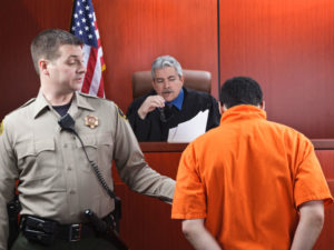 a bailiff holds a defendant's arm as the judge reads him the verdict in court